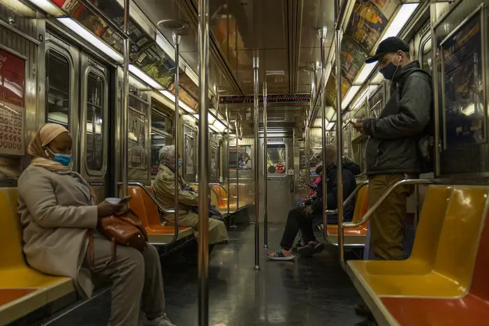 People, wearing masks, in a half empty subway car with orange and yellow seats